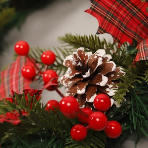 Couronne de Noël avec baies rouges, pommes de pin enneigées et feuilles à carreaux