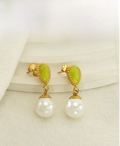 Détail macro de boucles d'oreilles avec pierre œil de chat verte et perle blanche