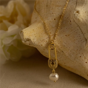 Close-up of golden safety pin necklace with pavé diamonds and a white pearl pendant