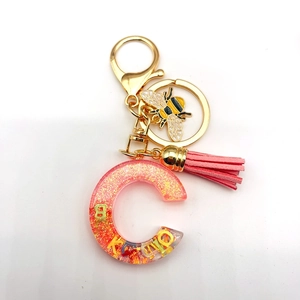 Detail of resin letter C keychain with gold bee charm and pink tassel for handbags