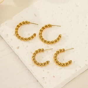 Minimalist gold twisted C-shape hoop earrings in two sizes on a textured white tray