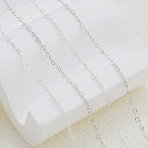 Detailed macro view of silver heart-shaped metal link chain on a clean white background