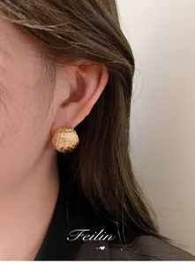 Close-up of golden textured hemispherical stud earrings on model for a luxury look