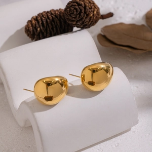 Minimalist gold pebble stud earrings in polished stainless steel on white plaster pedestal