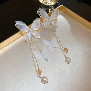 Close-up of butterfly earrings with white lace wings, golden tassels and pearl accents
