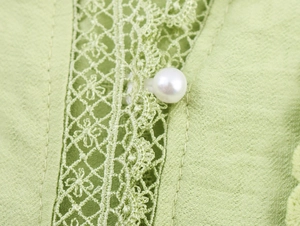 Detail of light green textured fabric with lace insert and a white pearl button