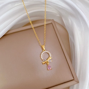 Close-up of golden necklace with sparkling bow pendant and pink teardrop gemstone