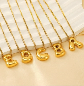Close-up of golden 3D bubble initial pendants on polished stainless steel cuban chains