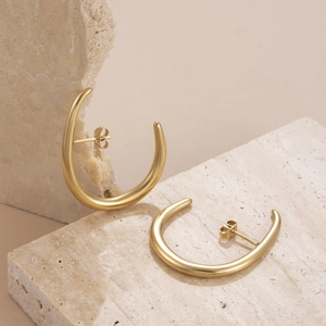 Minimalist gold C-shaped block tassel earrings on a textured stone display