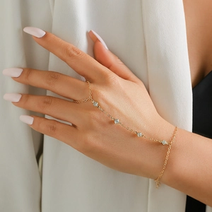 Detail view of a gold finger bracelet with rhinestones worn on a hand over a white suit