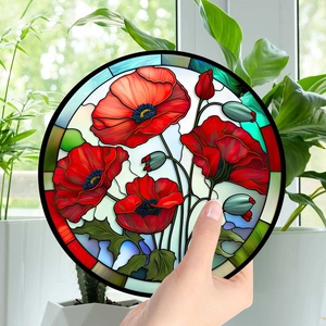 Close-up of circular acrylic suncatcher with red poppy pattern hanging in natural light