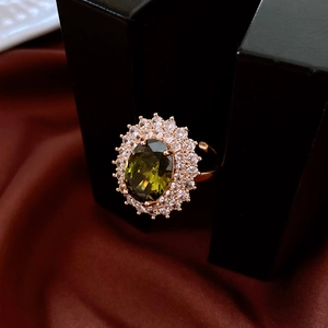 Close-up of olive green oval gemstone ring with crystal halo on red silk