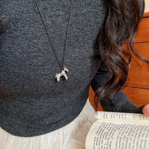 Detail of silver pony pendant necklace on model wearing dark knit sweater and beige skirt