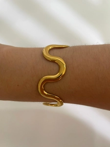Close-up of a wavy gold open bangle with a polished metallic finish on a model's wrist