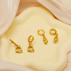 Close-up of golden dolphin heart and seashell earrings on beige silk background