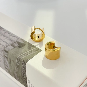 Detailed view of chunky gold huggie hoop earrings with polished finish on white gift box
