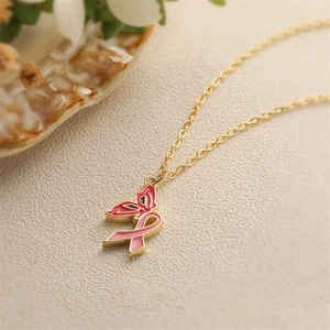 Golden necklace with pink enamel butterfly ribbon pendant on a natural background