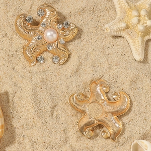 Detailed view of golden starfish earrings with pearls and rhinestones on beach sand