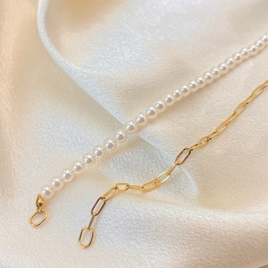 Elegant gold chain and pearl necklace displayed on white silk fabric background