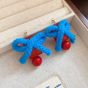 Detailed shot of bow-knot tassel earrings with red beads and blue woven texture