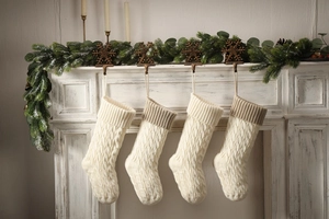 Four cable knit Christmas stockings in beige and khaki hanging on a festive mantelpiece