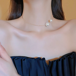 Detailed view of an elegant gold choker necklace with two white pearls on a model neck