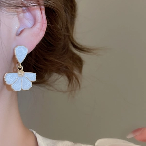 Gros plan de boucles d'oreilles fleur blanche avec bordure dorée portées
