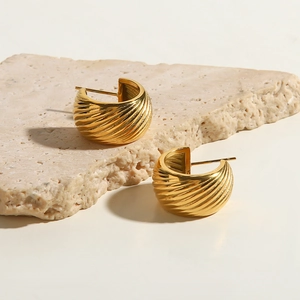 Close-up of golden C-shaped hoop earrings with spiral texture on a stone background