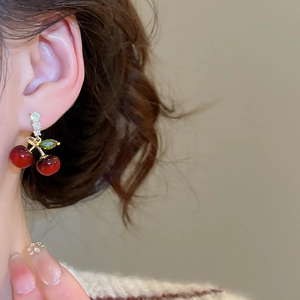 Détail de boucles d'oreilles cerise rouge avec tiges dorées sur le mannequin