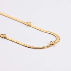 Golden flat snake chain necklace with three inlaid square clear zircon stones on white background