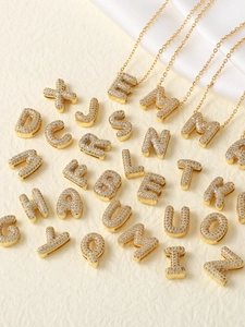 Macro shot of gold-plated alphabet necklaces with sparkling zircon pavé on beige silk fabric