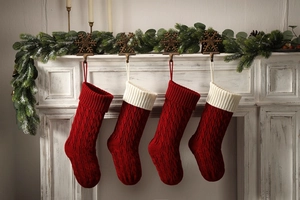 Close-up of four red knitted Christmas stockings with cable patterns hanging on mantel