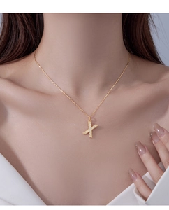 Detail of a sparkling gold X-shaped pendant necklace with pavé diamonds on a model
