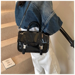 Detail view of the black glossy patent leather texture and silver buckles on messenger bag