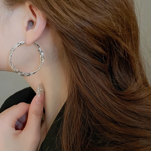 Macro detail of large silver geometric hoop earrings with textured lava finish on model