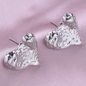 Macro view of silver heart earrings with lava texture on soft silk fabric background