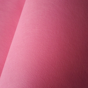 Macro detail of pink non-woven fabric showing dotted embossed texture and material layers