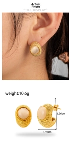 Macro detail of gold C-shape steel earrings with woven texture and white cat eye stone