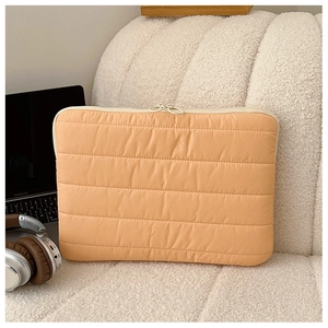 Detail of the orange quilted laptop sleeve on a soft sofa with cozy lifestyle props