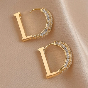 Detail of gold letter D earrings with white zircons on a luxury champagne silk background