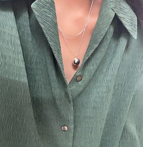 Close-up of minimalist layered 925 sterling silver chain necklace with bead pendant on model