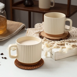 Beige ceramic coffee mugs with vertical stripes and clay base in cozy home setting