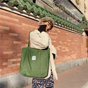 Detail of forest green canvas tote bag with white woven label on red brick background