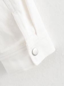 Close-up of white twill denim jacket sleeve featuring a polished silver metal button detail