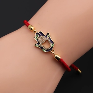 Macro detail of Hamsa Hand charm with blue enamel and zircons on red braided rope bracelet