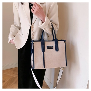 Detail of canvas tote bag with blue trim and removable strap held by a model in a suit