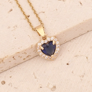 Macro shot of gold heart necklace with a deep blue center stone on beige stone base
