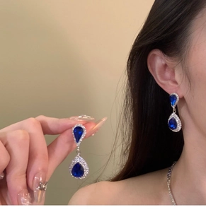 Close-up of teardrop dark blue gemstone earrings with sparkling crystal accents