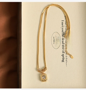 Macro detail of gold snake chain necklace featuring a heart zircon pendant on a beige box