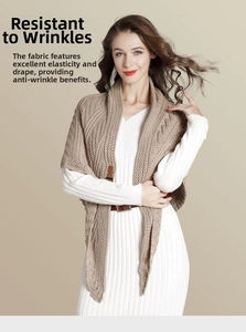 Detail of camel knit shawl with leather buckle closure over a white striped dress
